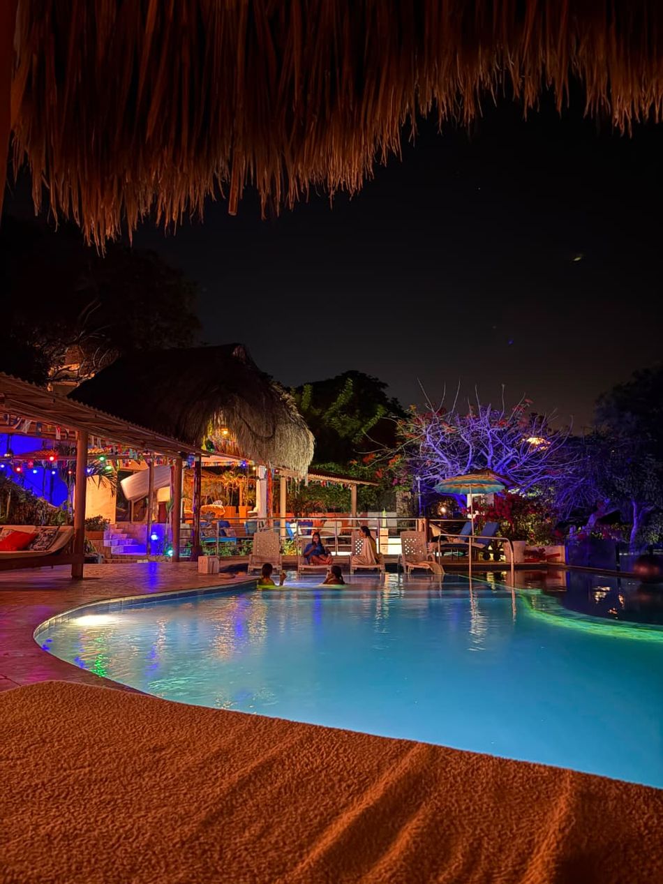Piscina iluminada de noche, bajo un techo de palma